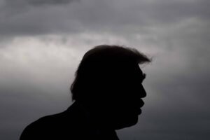 A imagem mostra a silhueta de uma pessoa contra um fundo de nuvens escuras e ameaçadoras. A figura tem um cabelo característico e está em perfil, com a boca ligeiramente aberta, sugerindo que está falando ou expressando algo. O ambiente parece sombrio devido à iluminação e às nuvens.