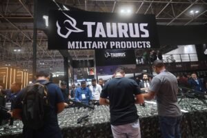 A imagem mostra um estande da Taurus, com uma grande faixa escrita