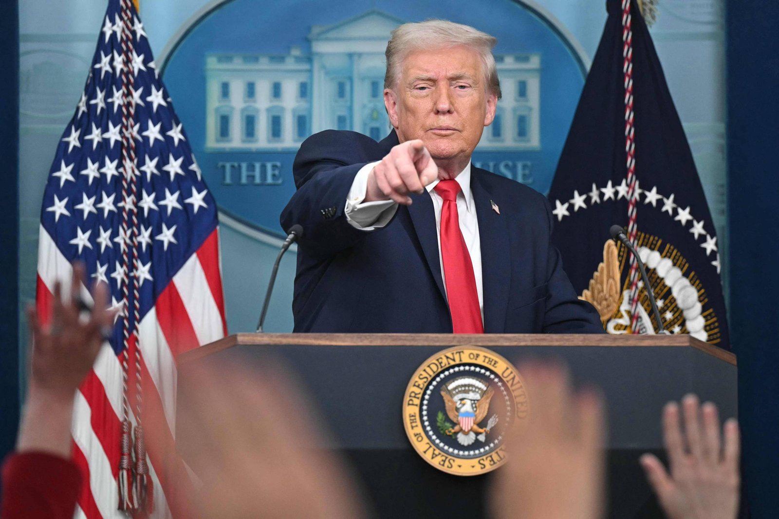 Ex-presidente dos Estados Unidos em púlpito na Casa Branca, apontando para a audiência. Bandeira americana e selo presidencial visíveis ao fundo.