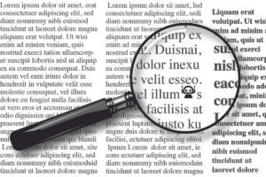Lupa com cabo preto posicionada sobre uma página com texto em colunas, ampliando parte do texto em fonte serifada. O texto ampliado mostra palavras em latim simulado, destacando letras e detalhes tipográficos.