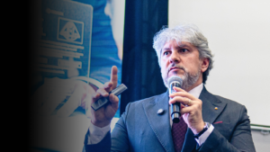 Luciano Menezes durante palestra, segurando microfone e fazendo gesto técnico, em ambiente corporativo, abordando estratégia fiscal e gestão empresarial.