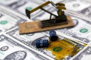 Miniatura de bomba de óleo em madeira sobre várias notas de dólar. Dois barris azuis com a palavra