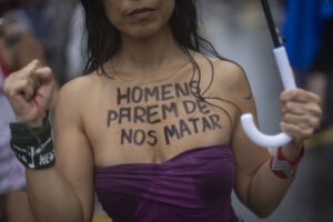 Mulher com blusa roxa sem alças exibe no peito a frase escrita